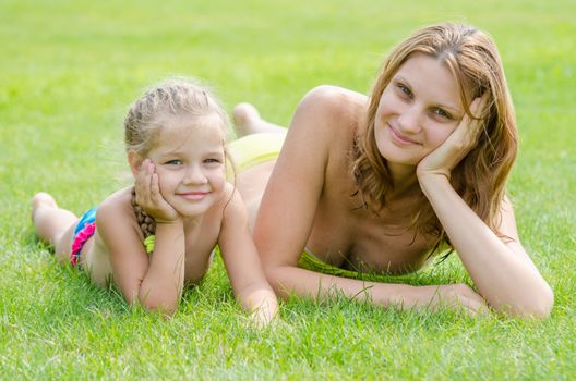 Young mother and five year old daughter lying on green grass and looking to the frame