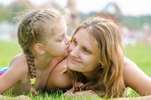 The five-year daughter kissing her mother lying on green grass lawn