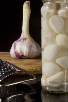 Marinated and fresh garlic with a grater on a dark background