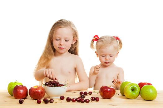 two little girls eat fruit at a table on the isolated background