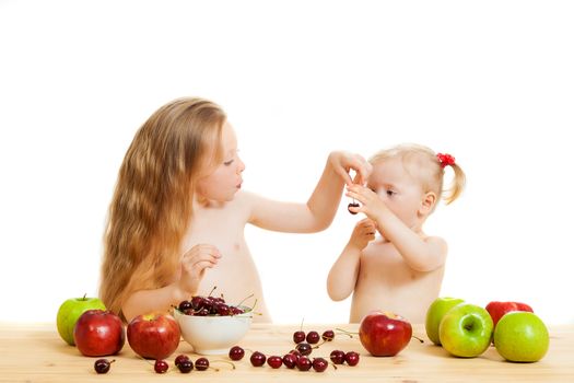 two little girls eat fruit at a table on the isolated background