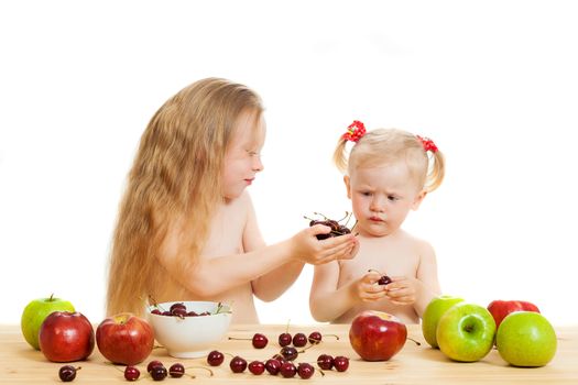 two little girls eat fruit at a table on the isolated background