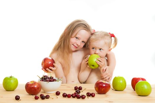 two little girls eat fruit at a table on the isolated background