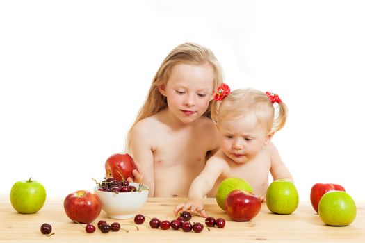 two little girls eat fruit at a table on the isolated background