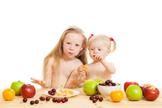 two little girls eat fruit at a table on the isolated background