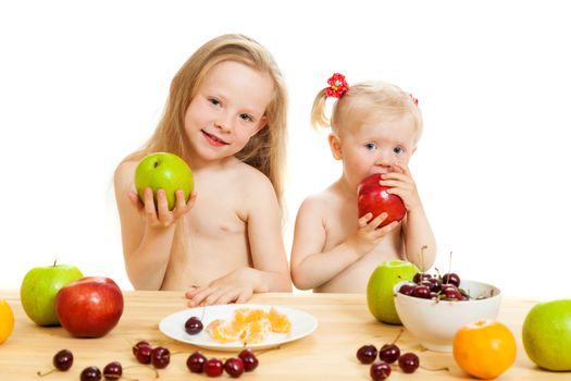 two little girls eat fruit at a table on the isolated background