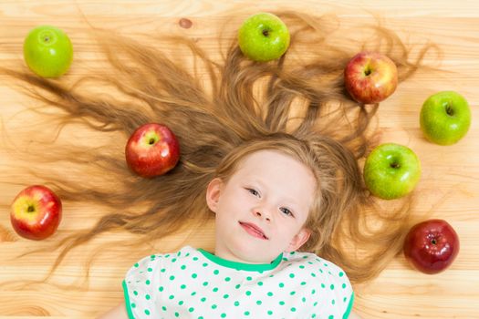 the little girl among apples on a wooden background