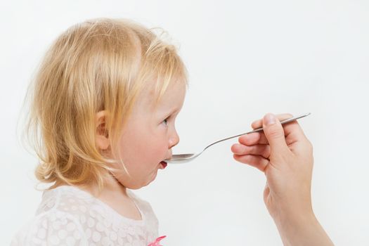 the little girl is spoon-fed on the isolated background