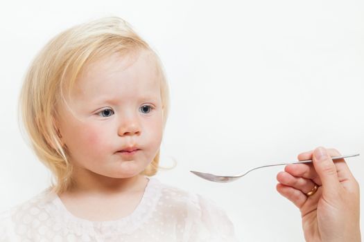 the little girl is spoon-fed on the isolated background