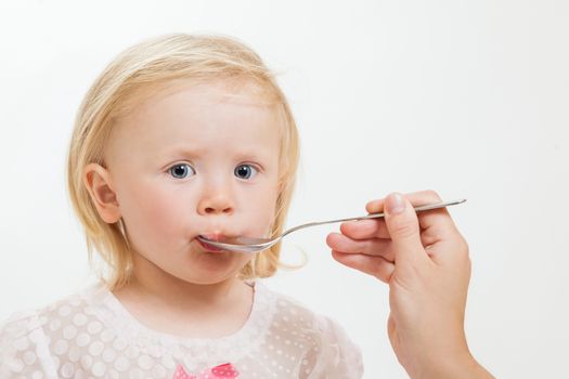 the little girl is spoon-fed on the isolated background