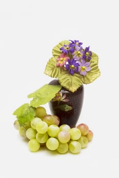 Porcelain vase with artificial flowers and green grapes on a white background