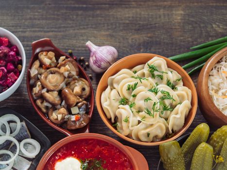 Russian food with copy space. Assortment dishes of Russian cuisine - borscht, pelmeni, herring, marinated mushrooms, salted cucumbers, vinaigrette, sauerkraut and pancakes. Top view or flat lay