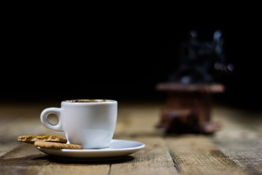 Freshly brewed coffee in mugs on a wooden table with a mill on a black background