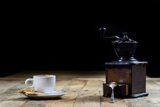 Freshly brewed coffee in mugs on a wooden table with a mill on a black background