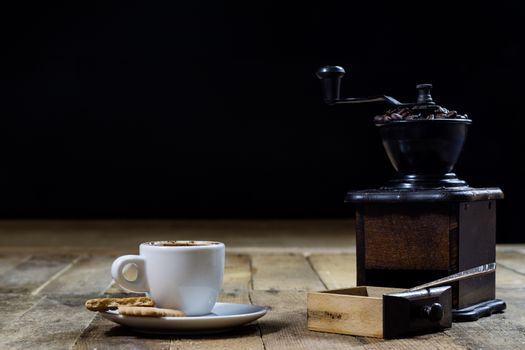 Freshly brewed coffee in mugs on a wooden table with a mill on a black background