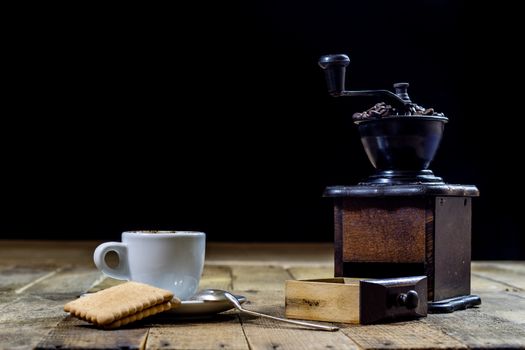 Freshly brewed coffee in mugs on a wooden table with a mill on a black background