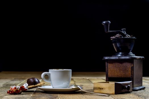 Freshly brewed coffee in mugs on a wooden table with a mill on a black background