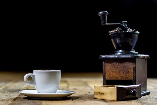 Freshly brewed coffee in mugs on a wooden table with a mill on a black background