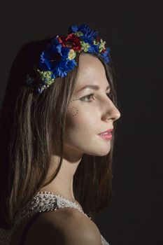 Portrait of a young woman in a wreath of flowers on a black background