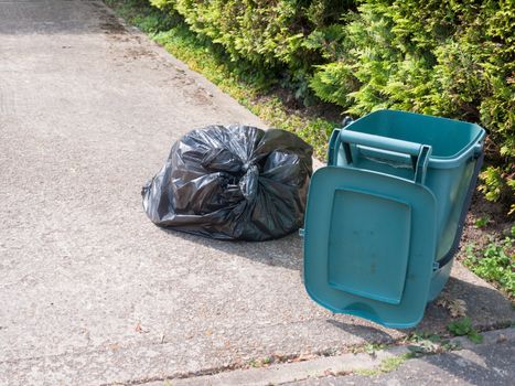 green food recycling bin open outside on front pavement with black tied bag