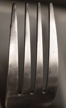 the top four prongs of a metal fork up close shining and reflecting in studio design graphic