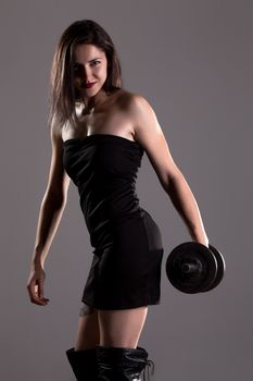 Sexy girl in short black dress, posing and lifting weights