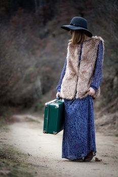 pretty young woman with a leather suitcase on a dirtroad in the mountains, vintage style