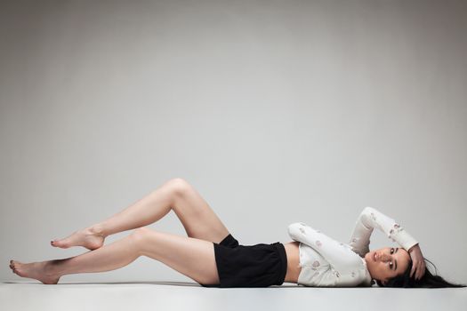 full body shot of beautiful black haired lady lying on the ground bare feet