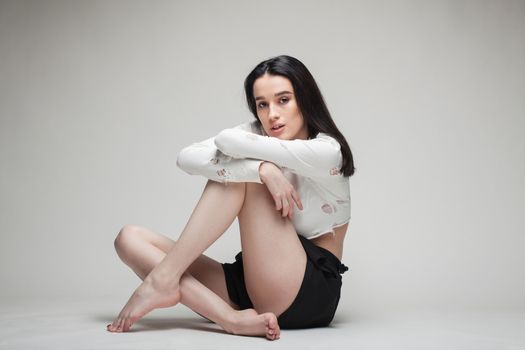 full body shot of beautiful black haired lady sitting on the ground bare feet