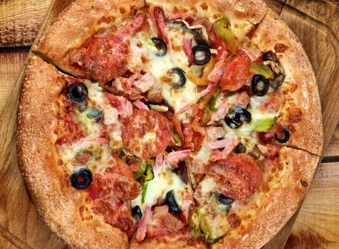 Freshly Baked Pepperoni Pizza with Black Olives, Ham and Cheese on Rustic Wooden background. Top View