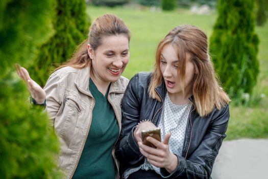 Two amazed women friends sharing social media in smart phone outdoors