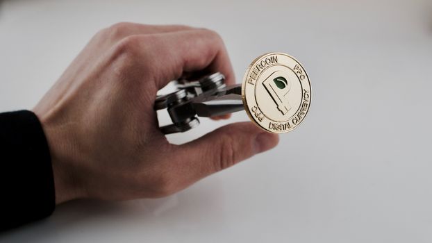 Digital currency physical gold peercoin coin in man hand. Pocket knife.