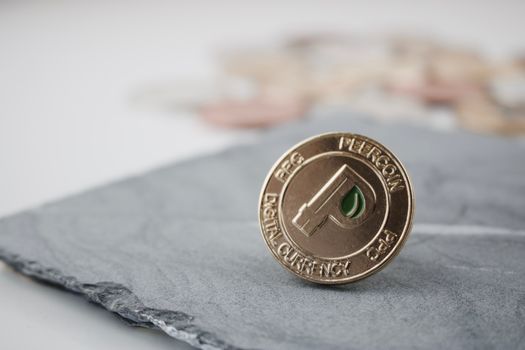 Digital currency physical gold peercoin coin with green leaf on the granite plate.