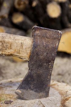 Close up shot of an axe in a stump with firewood in the background.