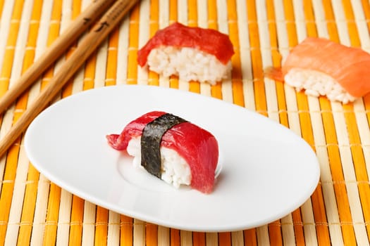  Red tuna Nigiri with Nori seaweed on white plate with chopsticks and other Nigiris. Raw fish in traditional Japanese sushi style. Horizontal image.