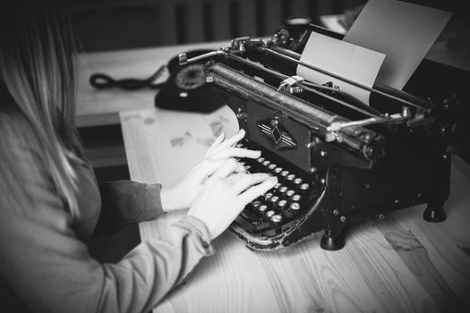 Secretary at old typewriter with telephone. Young woman using typewriter. Business concepts. Retro picture style. Black and white photography