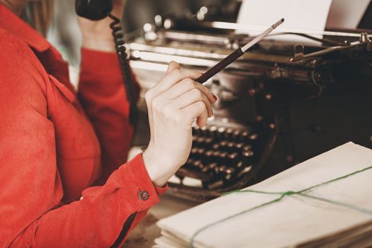 Secretary at old typewriter with telephone. Young woman using typewriter. Business concepts. Retro picture style.