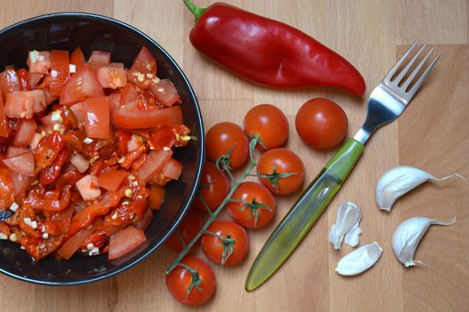 Tomato, roasted red pepper and garlic salad in a bowl with fresh vegetables and fork on a side