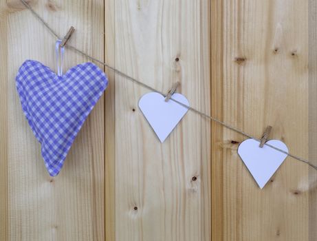 Three hearts with clothes pegs on a cord on wood