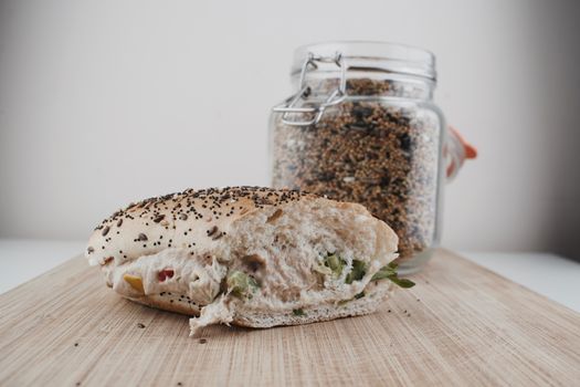 Tasty sandwich roll with a seeds, tuna, vegetables and salad near jar with seeds.