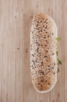 Long roll with seeds, tuna and salad on the wooden board in the kitchen.
