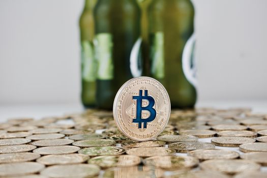 Cryptocurrency physical gold bitcoin coin on money near green beer bottles.