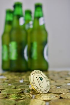 Digital currency physical gold peercoin coin with green leaf near green bottles.