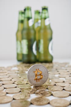 Cryptocurrency physical silver bitcoin coin near green beer bottles.
