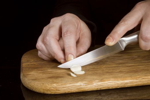 Woman chopping garlic with a knife on a wooden board