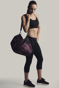 Portrait of sporty young woman posing with a gym bag,  against a gray background