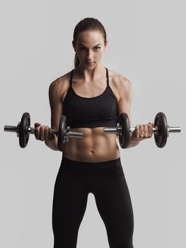 Beautiful young woman in a workout gear lifting dumbbells