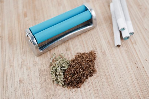Blue rolling machine, tobacco, joints and marijuana on the wooden board.