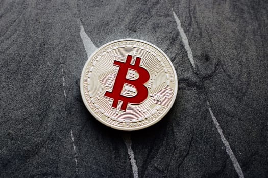 Digital currency physical silver bitcoin coin with red sign on the granite.