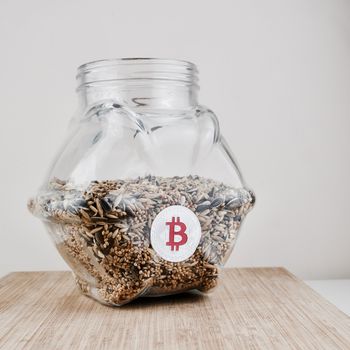 Digital currency physical silver bitcoin coin in glass jar with seeds.